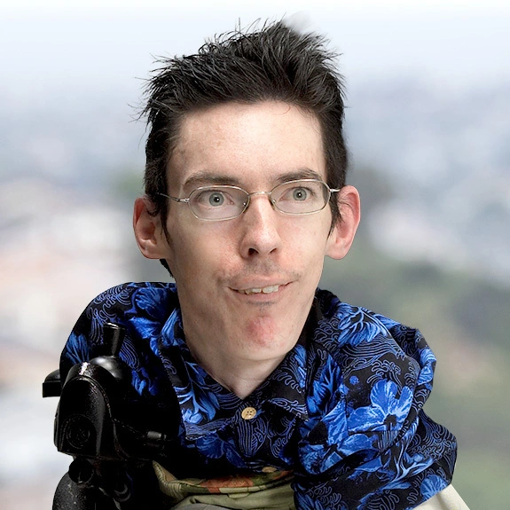 Photograph of Chris Van Deusen with glasses and a warm smile, standing outdoors with a soft-focus city view behind him.