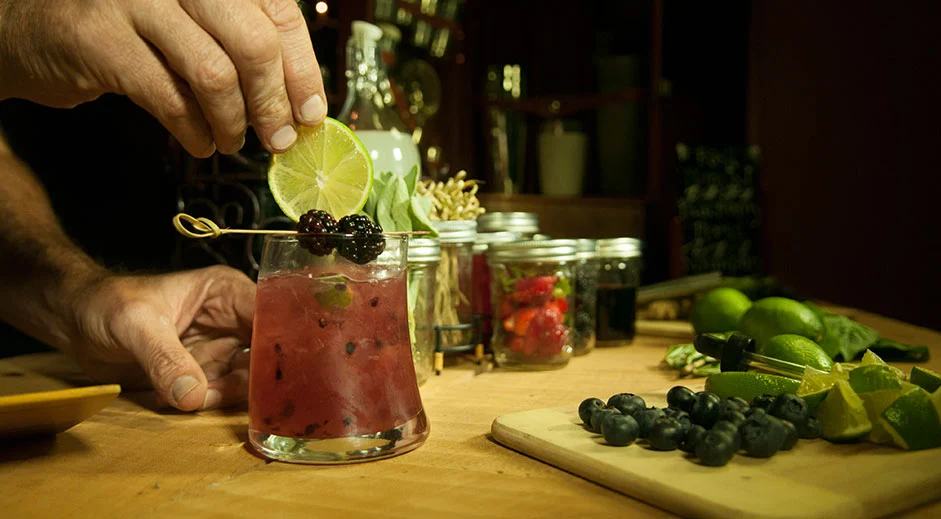 A bartender skillfully mixes a vibrant cocktail with fresh berries and lime at Paradise Bar, captured by Dogs of Design