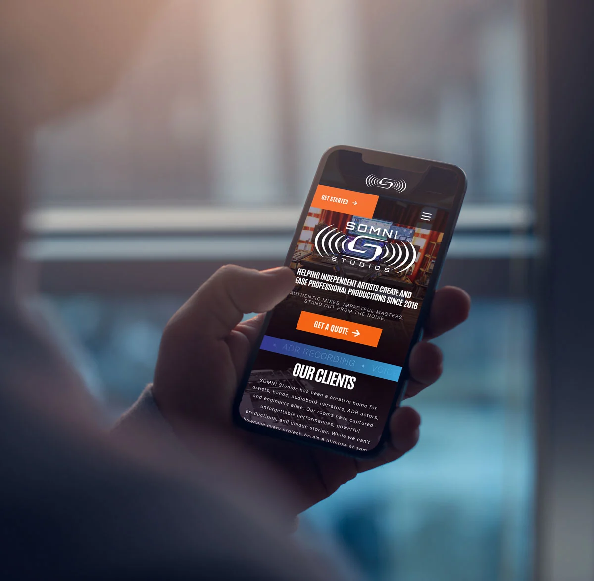 Person holding a smartphone displaying the Somni Studios website homepage with studio services and branding visible.