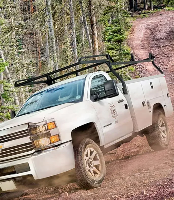 A white truck navigates a dusty road, showcasing the Rack-it Truck Rack, captured by Dogs of Design