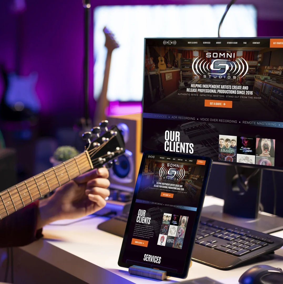 Somni Studios website shown on a desktop monitor and tablet inside a recording studio, with a musician holding a guitar in the foreground.